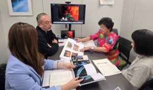 男女4人が書類や本が置かれた机を囲み話し合っている。